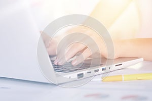 Woman`s hands typing on keyboard of notebook, sitting at table against white background, white lap top and yellow pen on desk,