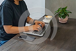 Woman`s hands typing laptop next to smartphone on wooden table