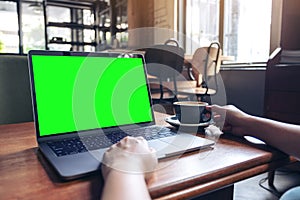 A woman`s hands using laptop with blank desktop screen while drinking hot coffee on wooden table in cafe