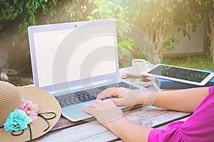 Woman& x27;s hands using laptop with blank screen on wooden table outdoors in the park
