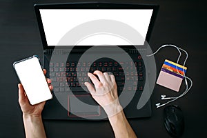 Woman`s hands using laptop keyboard and smartphone for shopping online while holiday sales. Top view of the workspace with credit