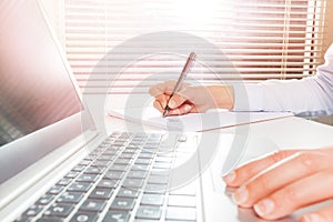 Woman`s hands using laptop and writing on notepad