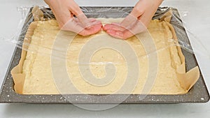Woman`s hands using plastic wrap unfurl pizza dough onto prepared baking pan. Homemade pizza