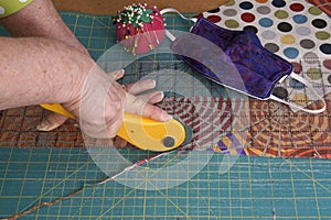 Woman`s hands using a rotary cutter to cut leftover quilting fabric for hand sewn face masks