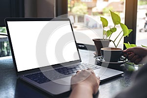 A woman`s hands using and touching laptop touchpad with blank white desktop screen while drinking coffee on wooden table in cafe