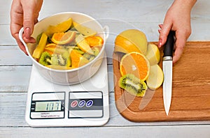 Woman`s hands weighing sliced fruits