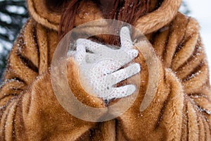 Woman`s hands in white knitted gloves close up. Woman in faux fur coat with snowflakes