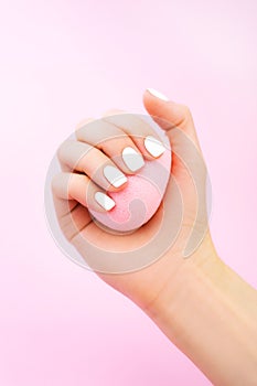 Woman`s hands with white manicure hold pink cosmetic sponge. Beauty spa salon concept. Trendy color nail gel polish