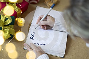 Woman`s hands in a white sweater write the plan for the year in the planner. Selective focus, bokeh lights, atmospheric photo.