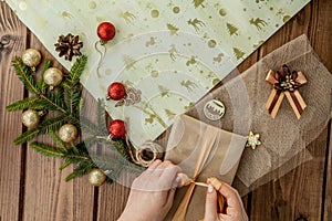 Woman s hands wrapping Christmas gift, close up. Unprepared christmas presents on wooden background with decor elements and items