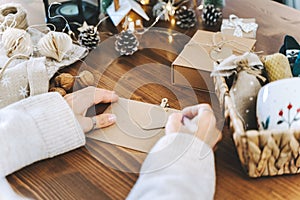 Woman s hands wrapping Christmas gift envelope, close up. Unprepared presents on white table with decor elements and