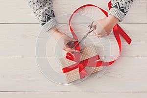 Woman`s hands wrapping christmas holiday present with red ribbon