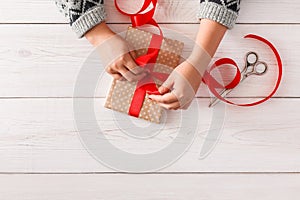 Woman`s hands wrapping christmas holiday present with red ribbon
