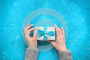 Woman`s hands wrapping a gift with a blue ribbon on a blue gange background. View from above. Beautiful Christmas and New Year