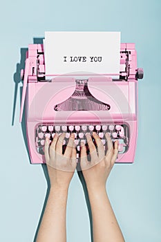 Woman`s hands writing `I love you` on an oldschool pink typewriter.