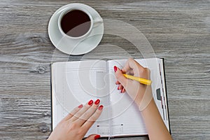 Woman`s hands writing information in a notepad. Cup of tea is on