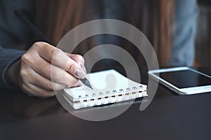 A woman`s hands writing on notebook with mobile phone on the table