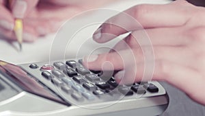 Woman's hands writing with a pencil and typing on a calculator