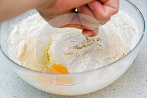 Woman`s hands with an yeast dough. The woman has added the yolk of a chicken egg and is stirring the baking dough in a glass bowl