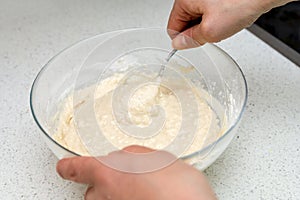 Woman`s hands with an yeast dough. The woman is stirring the baking dough in a glass bowl