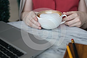 Woman`s handswith coffee cup and laptop for business on table, close up macro photo