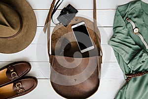 Woman's journalist or traveler accessories on white wooden table background flat lay. Brown leather purse, marine shoes, mobile