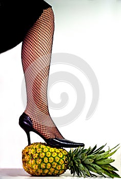 Woman's leg wearing heals and stocking standing on a pineapple