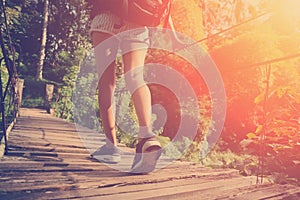 Woman`s legs with backpack walking across hanging bridge