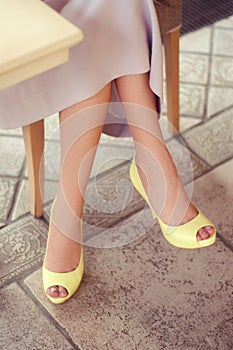 Woman's legs in light yellow open-toe pumps. Woman sitting in a