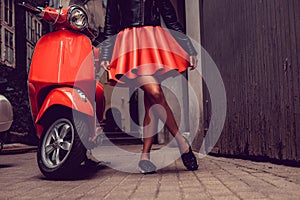 Woman`s legs near red motor scooter.