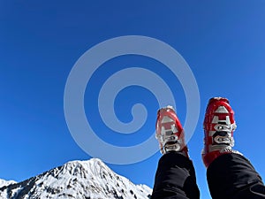 Woman& x27;s legs in red ski boots resting after a ski tour on sunny day, snowy Alps in the background.