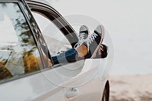 Woman`s legs in sneakers in the window car with road map. Girl in jeans in the car with her legs crossed.