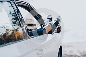 Woman`s legs in sneakers in the window car with straw hat. Girl in jeans in the car with her legs crossed.