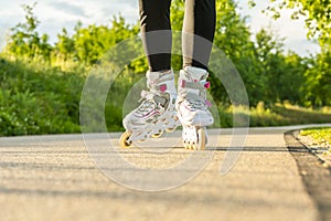 Woman`s legs with white roller blades at sunny day on asphalt road.