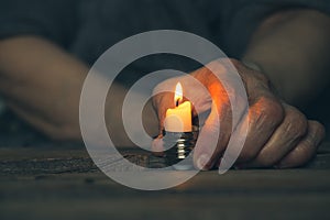 A woman's old hand holds a candle in a cartridge from a light bulb on a table at home in the dark without light, a