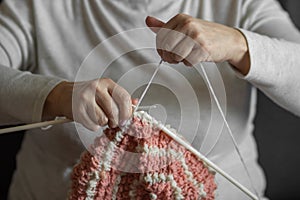 Woman& x27;s old hands knitting with needles warm beret hat. Grandma knit up with pink and white natural woolen threads.