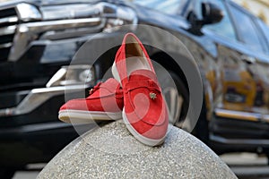 Woman's red stylish suede loafer shoes on a stone, car on a background. Pair of trendy female loafers shoes