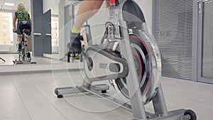 Woman`s reflection in the mirror in tracksuit on a stationary bike. Legs are spinning pedals on the stationary bicycle.