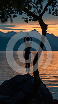 Woman\'s silhouette doing yoga against a sunset over a body of water, a woman on a rock practices a yoga pose under a tree