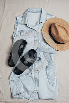 Woman& x27;s travel accessories: denim dress, straw hat, black sandals on grey background. Summer casual outfit. Flat lay