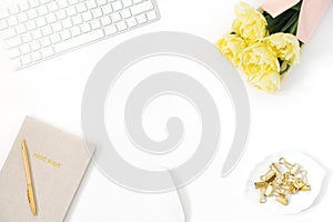 A woman`s workspace, working at home or in the office. Copy space for a blogger: keyboard, a bunch of yellow tulips, paper clips