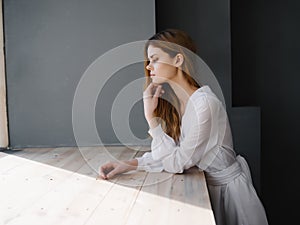 woman with sad facial expression white dress near luxury window