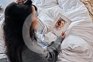 Woman, sad and photo for widow on bed after death, funeral or loss of husband, partner or man. Grief depression, girl