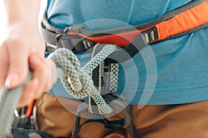 Woman in safety harness holding mountaineering rope knot eight, close-up.