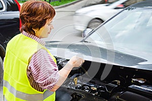 woman in safety vest stopped on street due to car breakdown, open hood, waiting for assistance