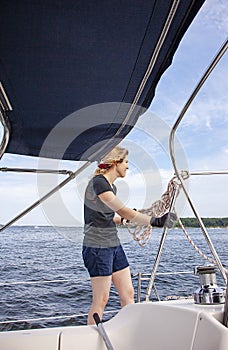 Woman sailing holding ropes to adjust sails on sailboat