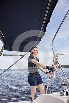 Woman sailing holding ropes to adjust sails on sailboat