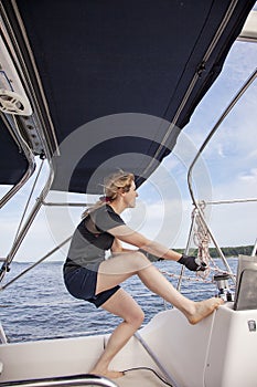 Woman sailing pulling ropes to adjust sails on sailboat