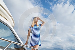 Woman sailor stands on deck yacht with striped dress and cap looks