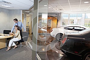 Woman and salesman sitting in car showroom office